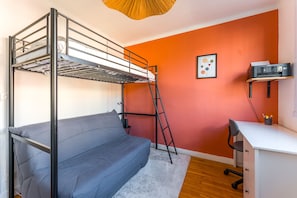 Ein Stockbett mit Schreibtisch und Stuhl, ein Drucker sowie ein gerahmtes Bild an der Wand.
