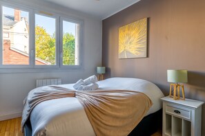 Ein Hotelzimmer mit einem großen Bett, zwei Nachttischen, einem Fenster und einem an der Wand hängenden Kunstwerk.