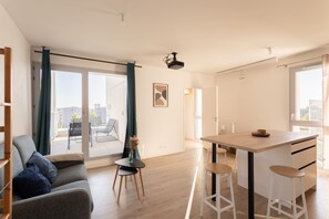A modern living room with a sofa, a small table with a vase, and a kitchen area with a bar stool. - Nouveau regard - Charmant appart avec Balcon (Rennes)