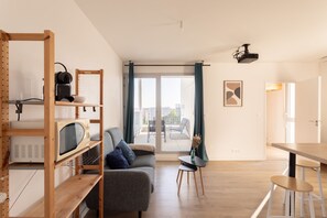 A modern living space with a sofa, a dining table, a kitchen area with a microwave, and a balcony with a view. - Nouveau regard - Charmant appart avec Balcon (Rennes)