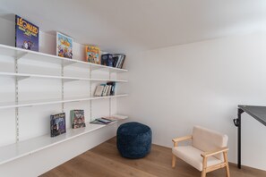 Une pièce avec une bibliothèque, un pouf bleu rond et une chaise en bois.