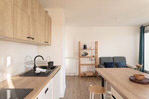 A modern kitchen with wooden cabinets, a black sink, and a wooden dining table with a chair. - Nouveau regard - Charmant appart avec Balcon (Rennes)
