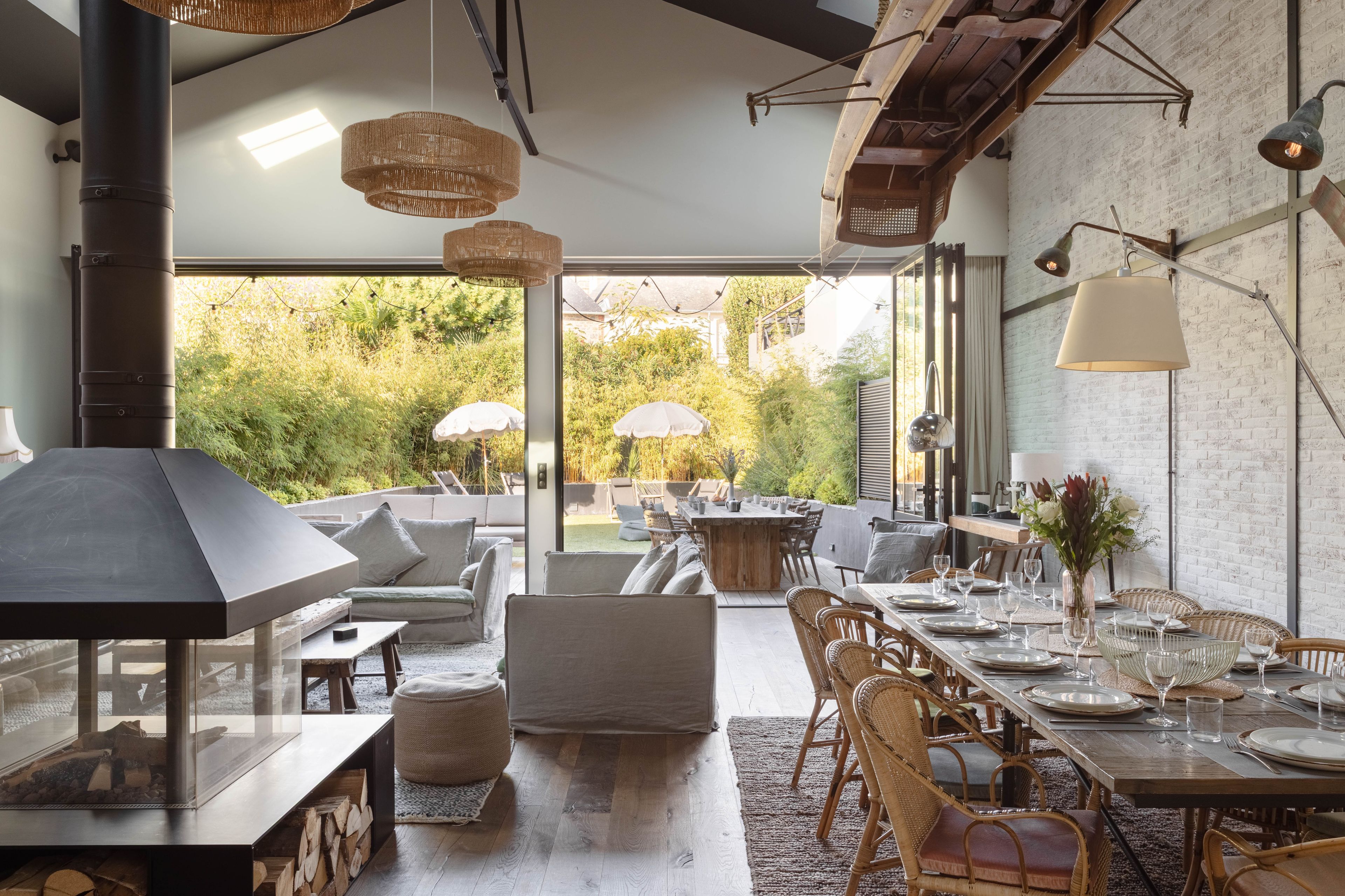 A spacious outdoor dining area with a view of greenery, furnished with wicker chairs and a wooden table set for dining.
