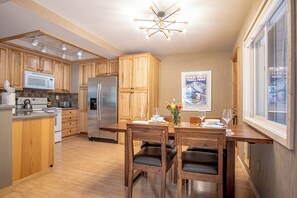 Una cocina moderna con armarios de madera, un refrigerador de acero inoxidable y un comedor con mesa dispuesta para dos.