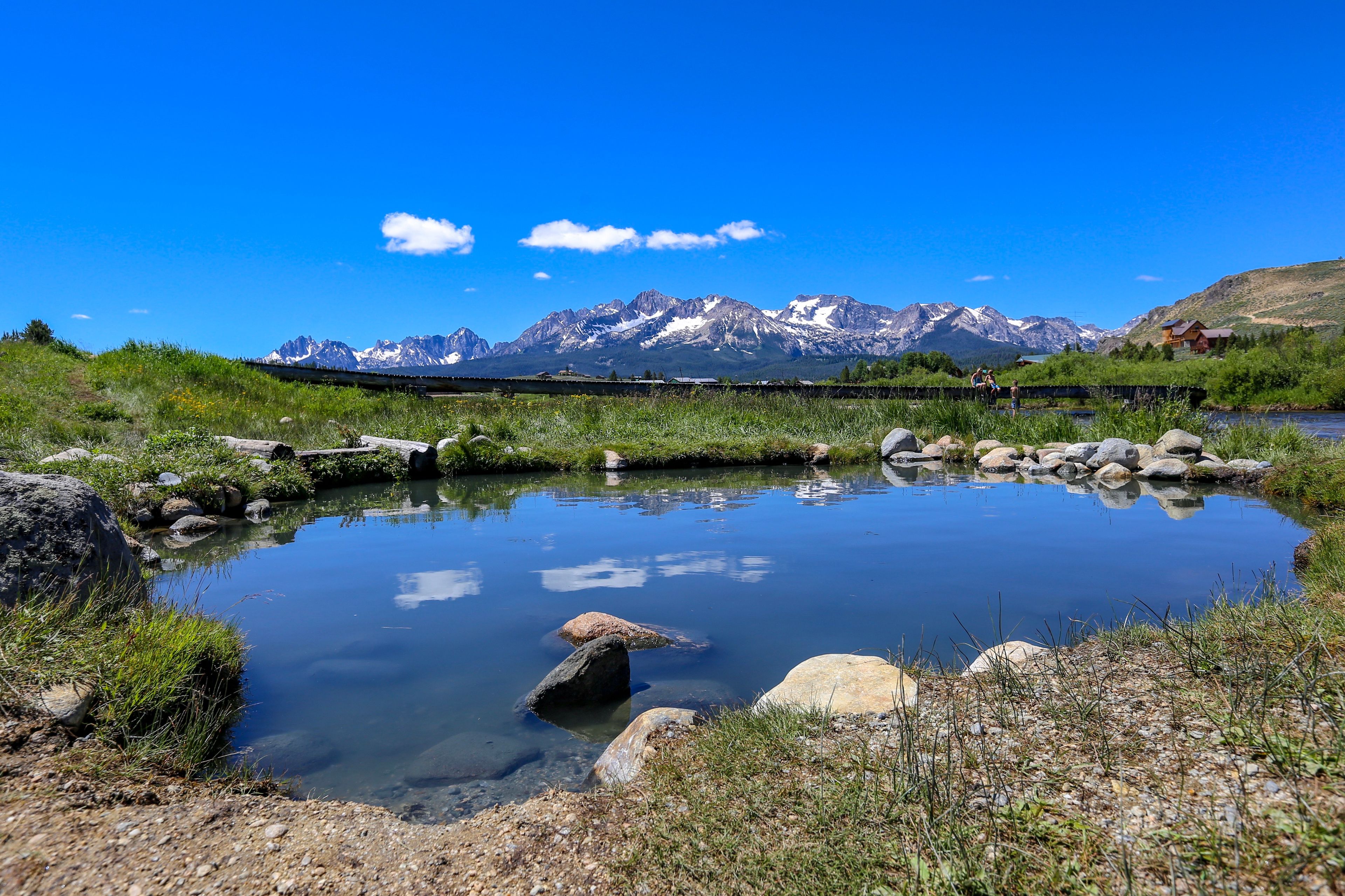 A serene mountain landscape with a clear lake, rocky shore, and a distant mountain range.