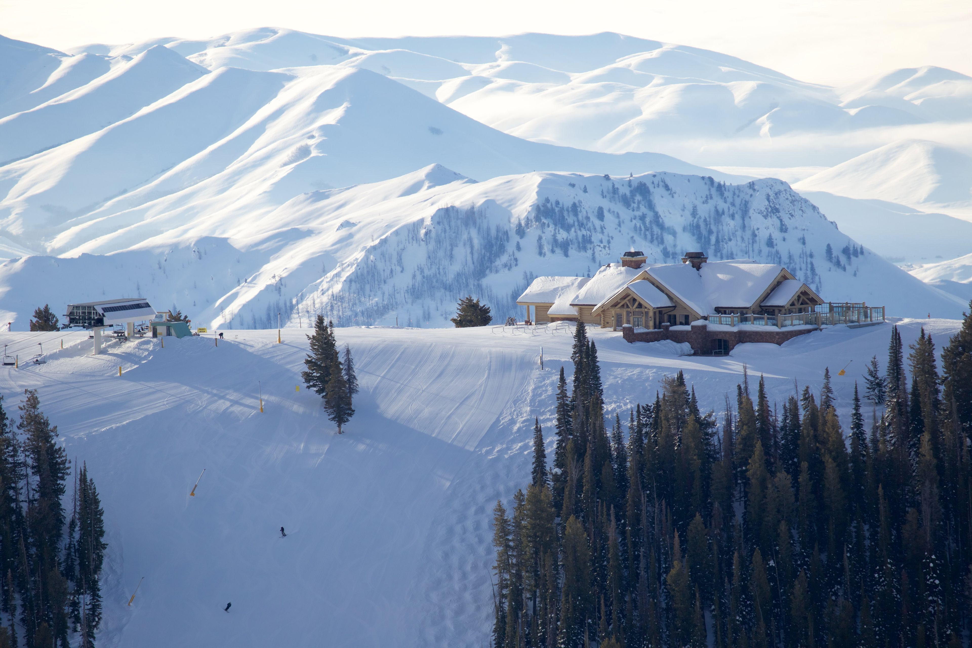 A snow-covered mountain with a lodge featuring a wooden exterior and a ski lift in the background.