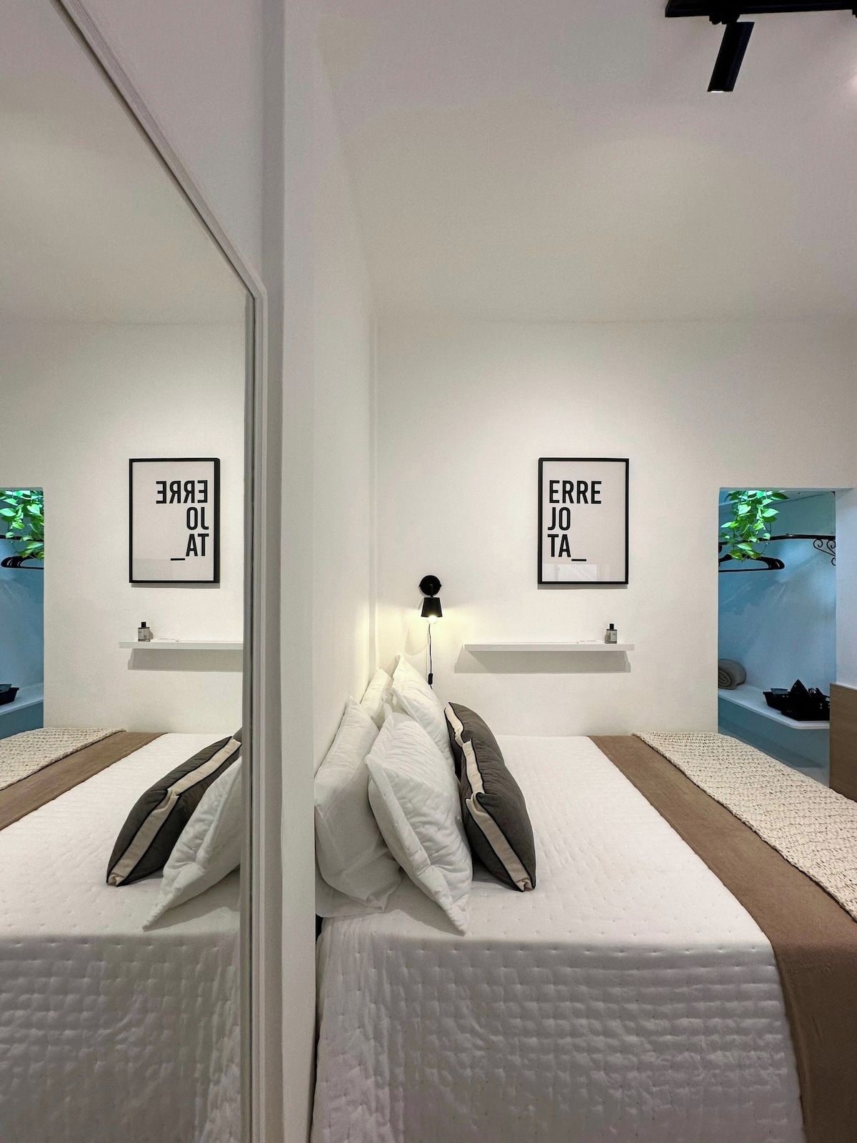 Un dormitorio moderno con dos camas, un espejo y dos luces fijadas a la pared.