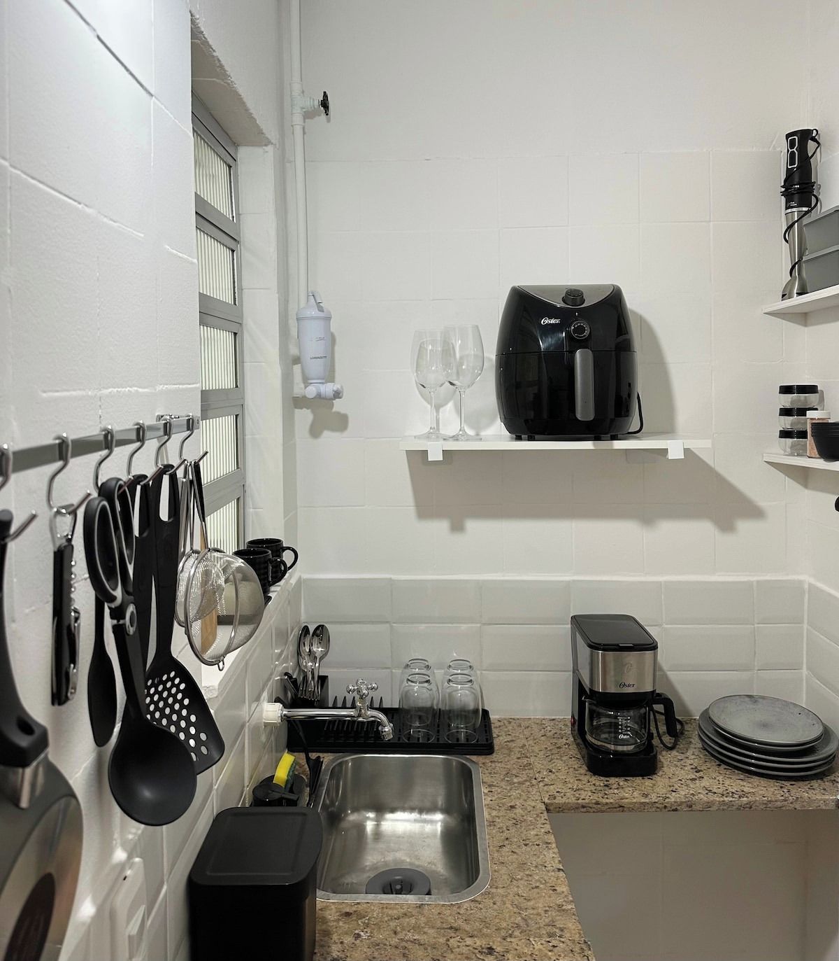 Een keuken met een roestvrijstalen spoelbak, een koffiezetapparaat en een zwart elektrisch waterkoker.