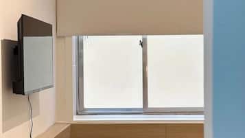Una habitación pequeña con una televisión montada en la pared, una mesa redonda con sillas y una ventana con persianas.