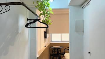 Una habitación compacta con cama, una mesita pequeña y sillas, una planta colgante y una toalla en el suelo.