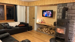 A cozy living room with a fireplace, a television mounted on the wall, and a stack of firewood. - CHALET MONTAGE, a renovated former farmhouse located between the Arve Valley and the ski resorts (Glières-Val-de-Borne)