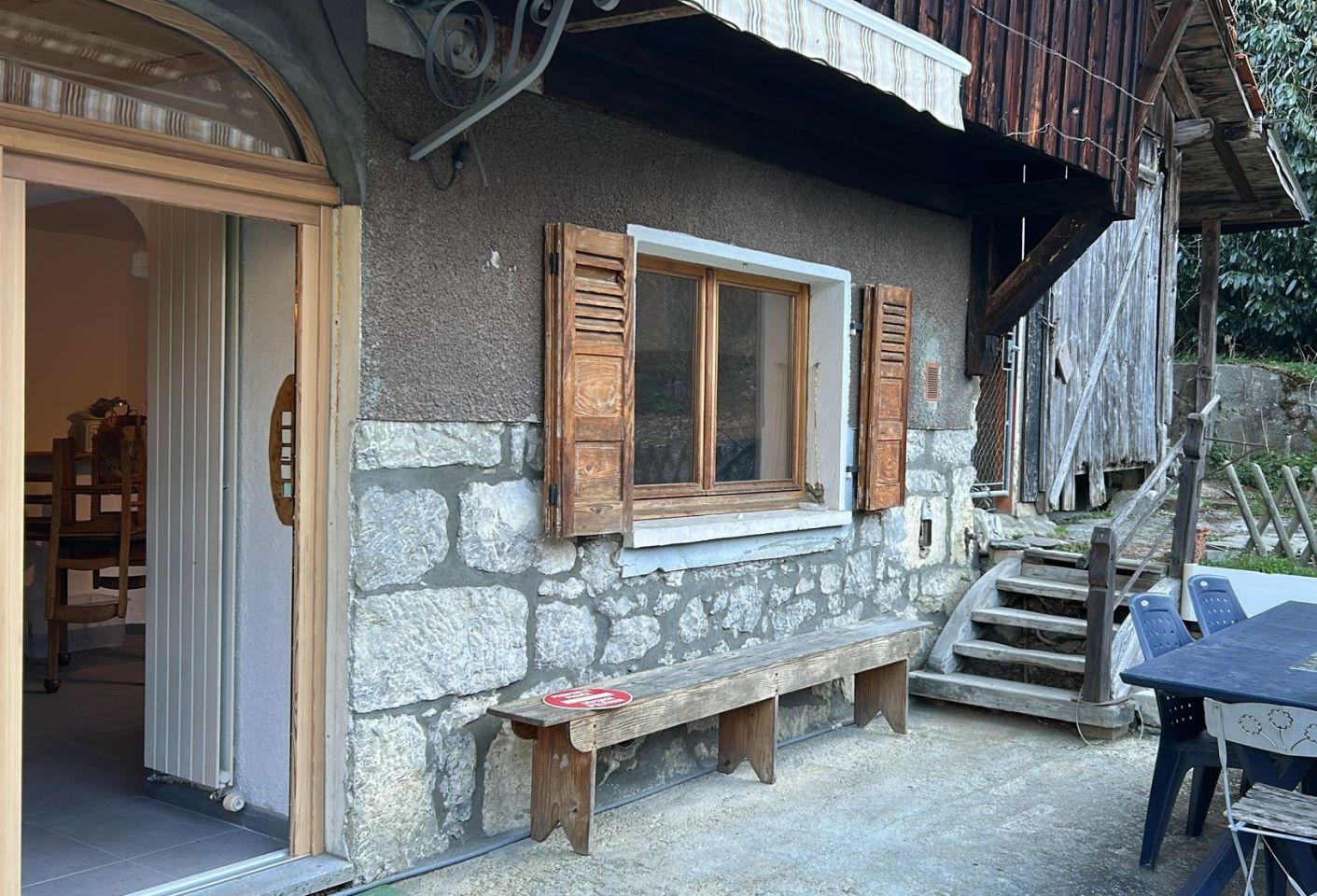 A rustic stone building with a wooden bench outside, a table, and a staircase leading to a wooden deck.
