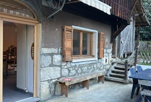A rustic stone building with a wooden bench outside, a table, and a staircase leading to a wooden deck. - CHALET MONTAGE, a renovated former farmhouse located between the Arve Valley and the ski resorts (Glières-Val-de-Borne)