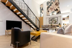 Ein modernes Wohnzimmer mit Treppe, Flachbildfernseher, Essbereich mit Stühlen und einer Couch.