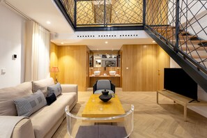 A modern living room with a sofa, coffee table, and a TV. There is a staircase with a metal railing leading to an upper level. - Genteel Home Reyes Catolicos Sevilla (Seville)