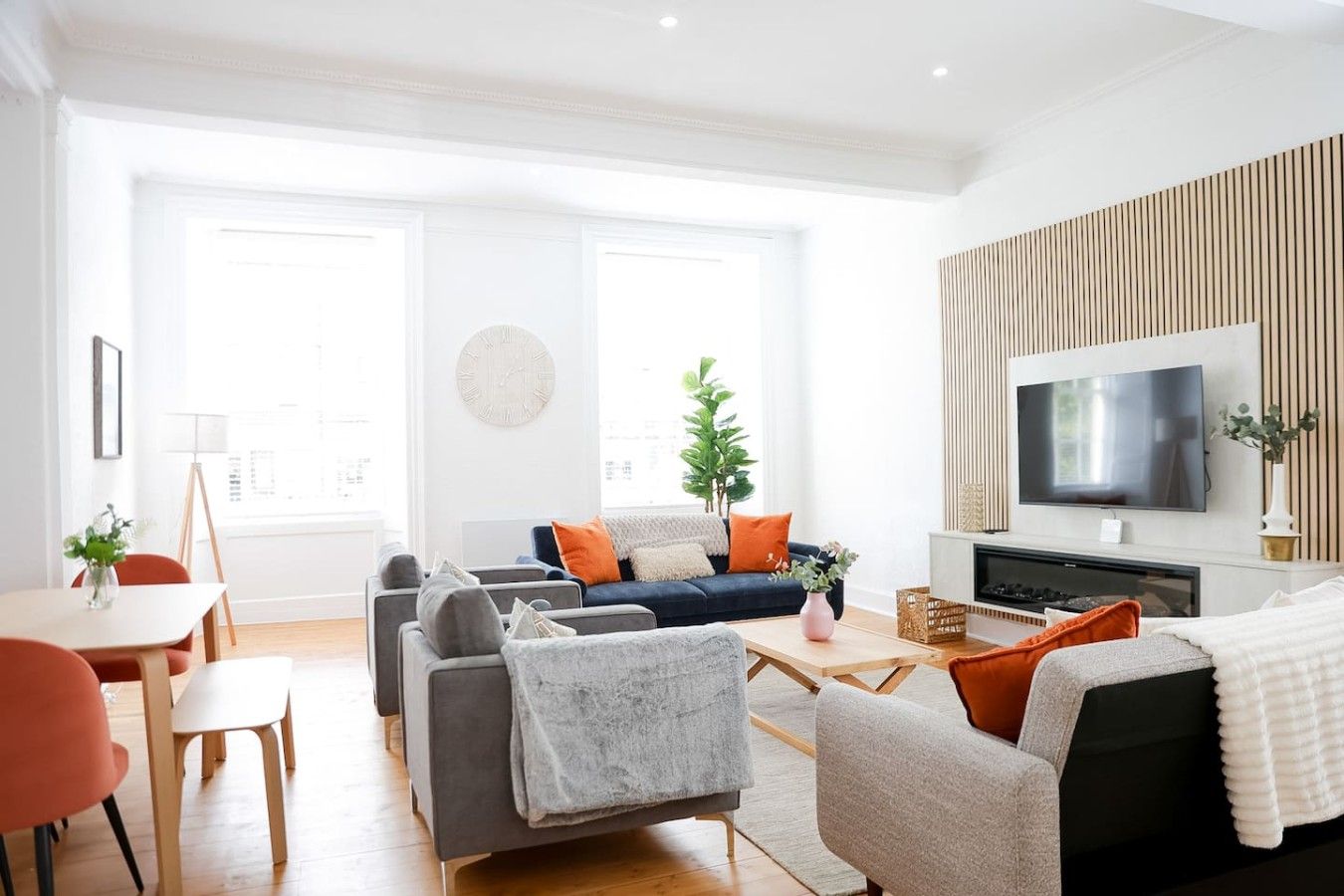 Un salon moderne avec un canapé, des fauteuils, une table basse et un téléviseur fixé au mur.