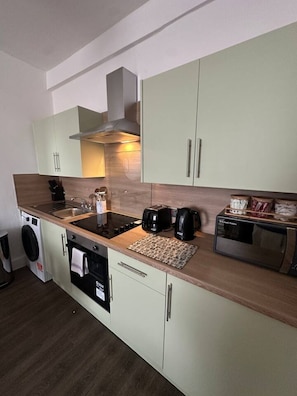 A compact kitchen with a washing machine, a microwave, and a coffee maker. - Cosy 1 BDR top floor apartment in leith (Edinburgh)