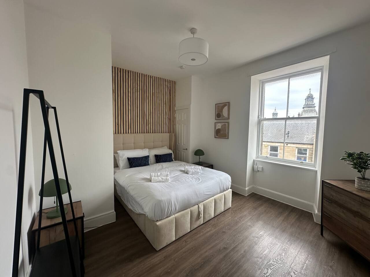 Une chambre à coucher avec un grand lit, une fenêtre donnant sur un immeuble, une table de chevet et une lampe.