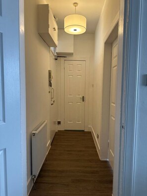 A narrow hallway with a wooden floor, white walls, and a white door at the end. - Cosy 1 BDR top floor apartment in leith (Edinburgh)