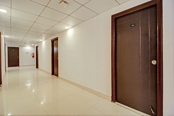 A corridor with tiled flooring, wooden doors, and a fire extinguisher on the wall. - Hotel O Qualia Miyapur (Hyderabad)