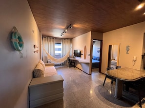 Una habitación de hotel moderna con techo de madera, una hamaca, un televisor de pantalla plana, un escritorio y un baño visible a través de una puerta abierta.