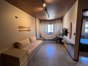 Una habitación con sofá, una mesita, una hamaca, televisor y ventana con cortinas.
