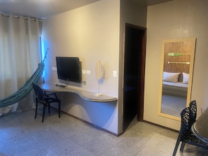 Habitación de hotel con televisor de pantalla plana, escritorio, silla, hamaca, cama con vistas y espejo.