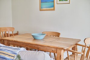 A wooden dining table with a blue bowl, surrounded by wooden chairs, in a room with a plain wall and a framed picture above. - Host and Stay | The Cottage  ALN (Lesbury)