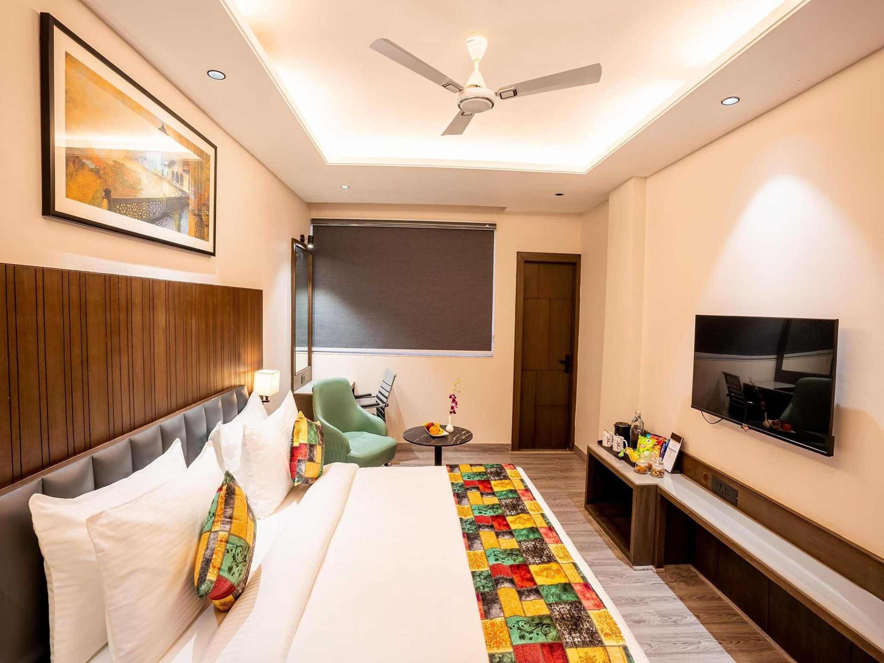 A hotel room with a bed, a television, a ceiling fan, and a window.