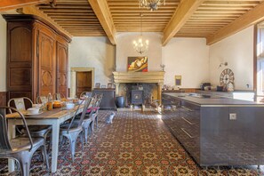 Een ruime kamer met een eettafel gedekt voor een maaltijd, een open haard en een keukenhoek.