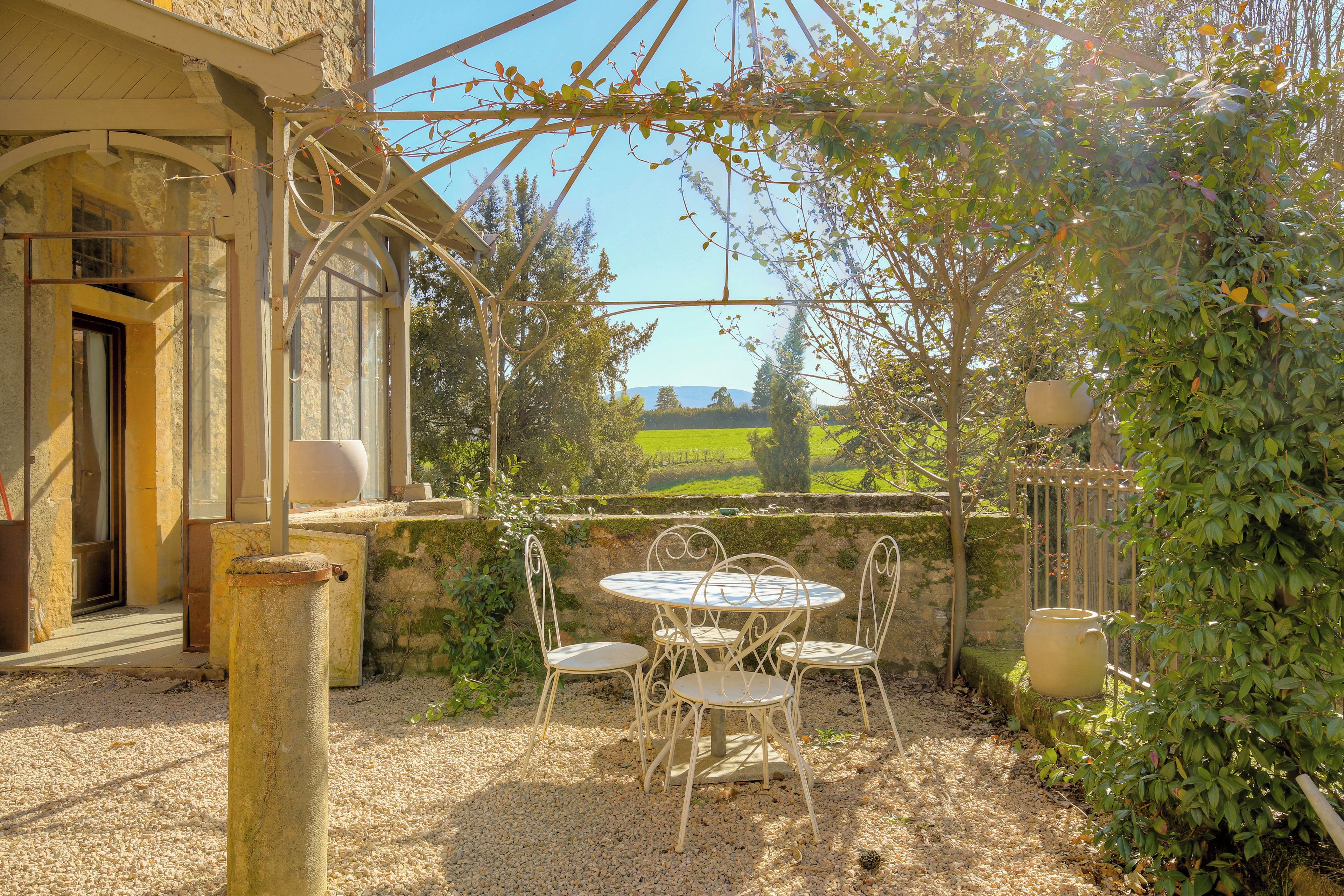 A patio with a table and chairs, a pergola, and a view of a green landscape.