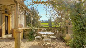 A patio with a table and chairs, a pergola, and a view of a green landscape.