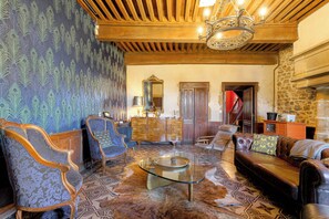 A room with a patterned wallpaper, a chandelier, a wooden ceiling, and a leather sofa. - The Château du Mas, near Lyon (Bessenay)