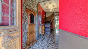 Un couloir avec des carreaux de sol à motifs, une porte en bois dotée d’un panneau de verre et un escalier avec un mur rouge d’un côté.