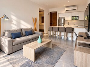 A modern living room with a sofa, coffee table, and a kitchen area with a refrigerator and bar stools. - Rooftop Pool Condo Steps from 5th Avenue (Playa del Carmen)
