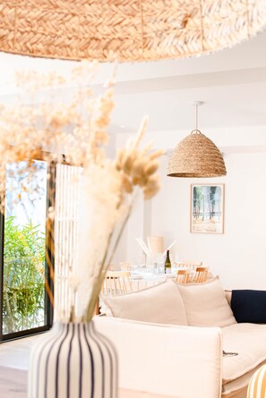 Ein modernes Wohnzimmer mit einer Couch, einem Esstisch und einer hängenden gewebten Leuchte.