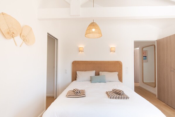 Ein Schlafzimmer mit einem großen Bett, zwei Wandleuchten, einer gewebten Deckenleuchte und einem Spiegel an der Wand.