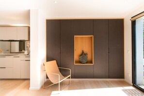 En modern inredning med en minimalistisk design, med en hylla med träram och ett dekorativt föremål, en stol med metallram och ett köksområde i bakgrunden.