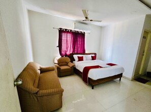 A bedroom with a bed, two chairs, a ceiling fan, and a window with curtains. - Classic Srinivasa Home Stays (Hyderabad)