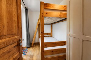 A bunk bed with a wooden frame and white bedding, a door with a brass handle, and a colorful rug on the floor. - NEW! Apartment Alpage | Large Terrace (Les Houches)