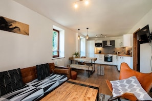 A modern kitchen with white cabinets, a dining area with a wooden table and benches, and a living area with a sofa and a coffee table. - NEW! Apartment Alpage | Large Terrace (Les Houches)