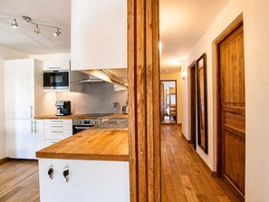 A modern kitchen with wooden countertops, stainless steel appliances, and a view into a bedroom through an open door. - NEW! Apartment Alpage | Large Terrace (Les Houches)