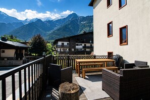 Een terras met een houten tafel en rieten meubilair, met uitzicht op een bergketen.