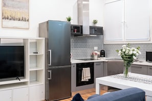 A modern kitchen with a built-in refrigerator, oven, and microwave. There is a dining area with a table and chairs, and a TV on a stand. - Vrbo Property (Rovigo)