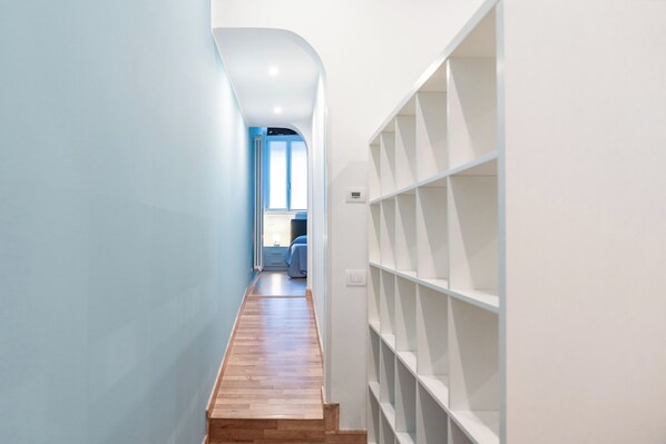 A narrow hallway with wooden flooring, a built-in shelving unit on the right, and a bed with a window at the end. - Vrbo Property (Rovigo)