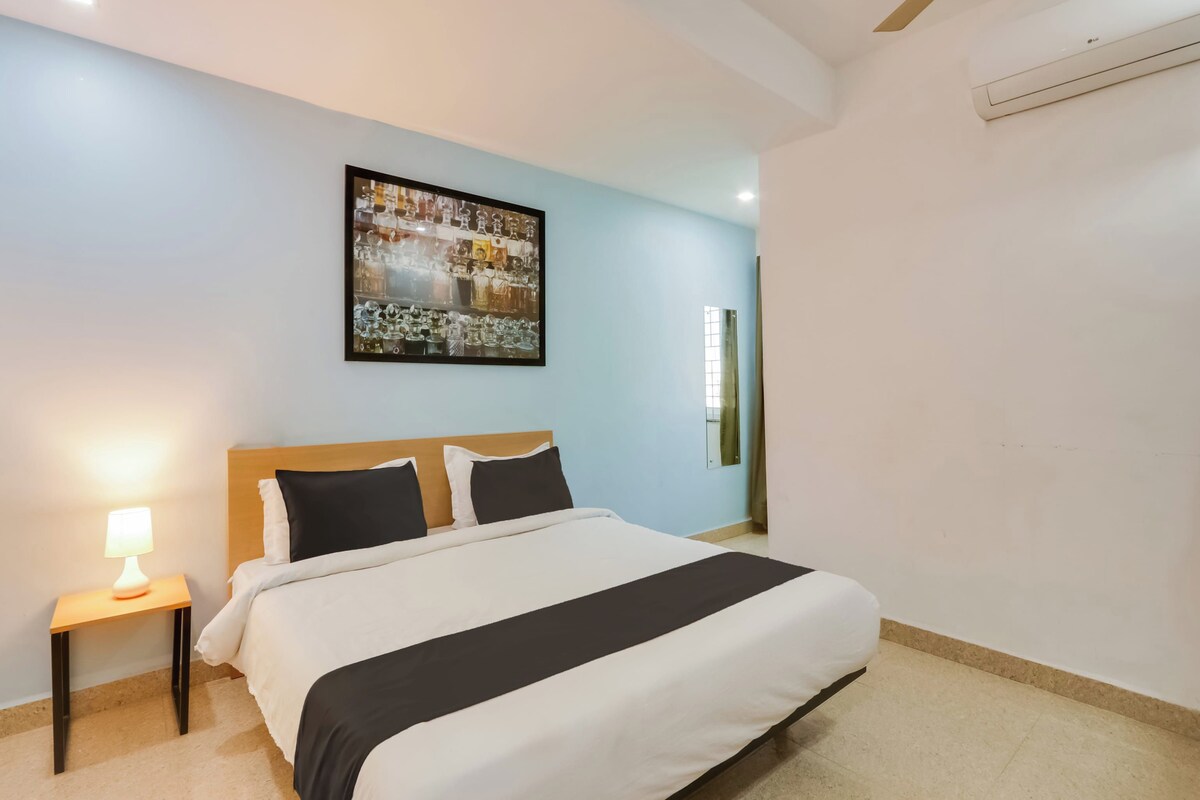 Habitación de hotel con una cama, una mesita de noche con lámpara, un ventilador de techo y un equipo de aire acondicionado instalado en la pared.