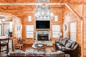 Ein Innenraum einer Blockhütte mit Kamin, Ledersofa und an der Wand montiertem Fernseher.
