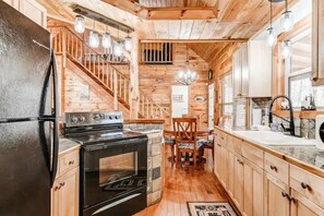 A wooden interior with a kitchen, dining area, and staircase. - Wooded Wonder | Creek + Hot Tub + Game Room (Cleveland)