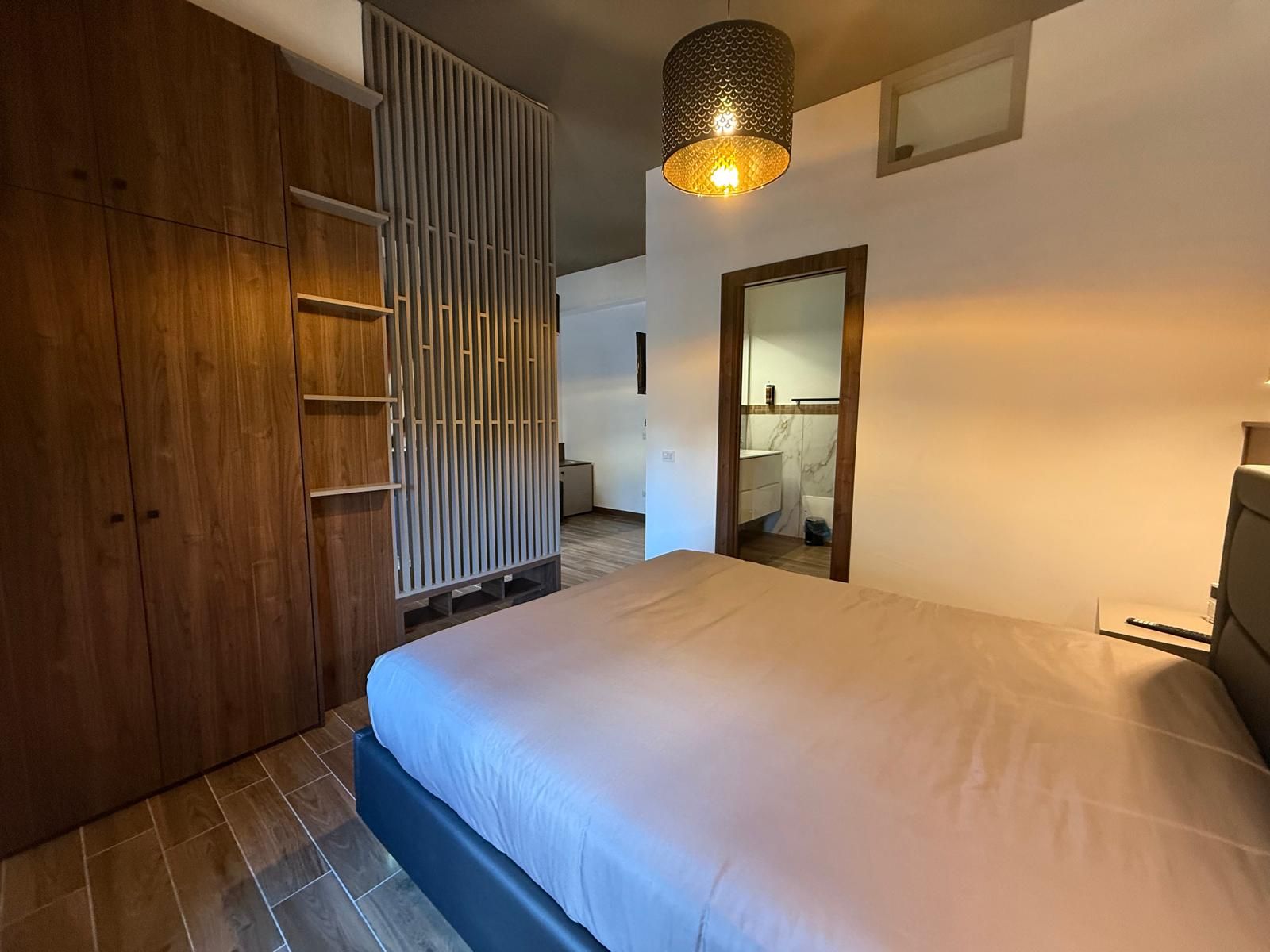 A bedroom with a bed, a wardrobe, a mirror, and a hanging light fixture.
