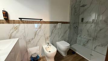 A bathroom with a marble wall, a shower enclosure, a bidet, and a toilet.